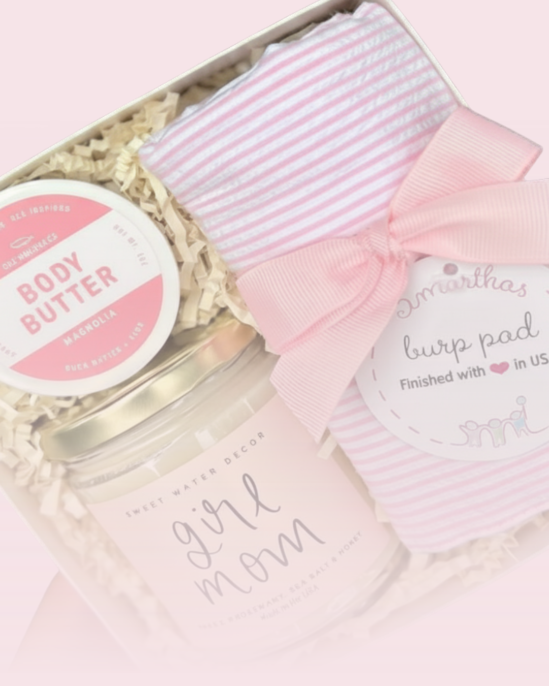Gift set with body butter, burp pad, and pink bow on a light pink background