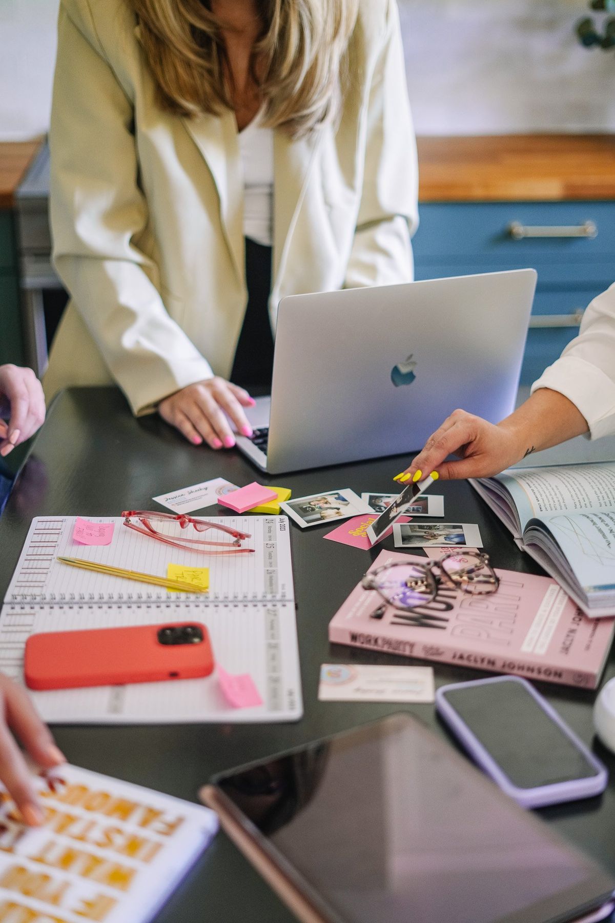 Two people working at a desk with a laptop, phone, and various items.